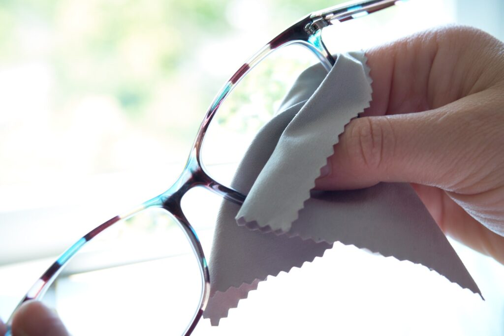 Person using lens cleaning solution and microfiber cloth on eyeglasses